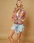 Woman wearing a colorful quilted vest and denim shorts on a beige background