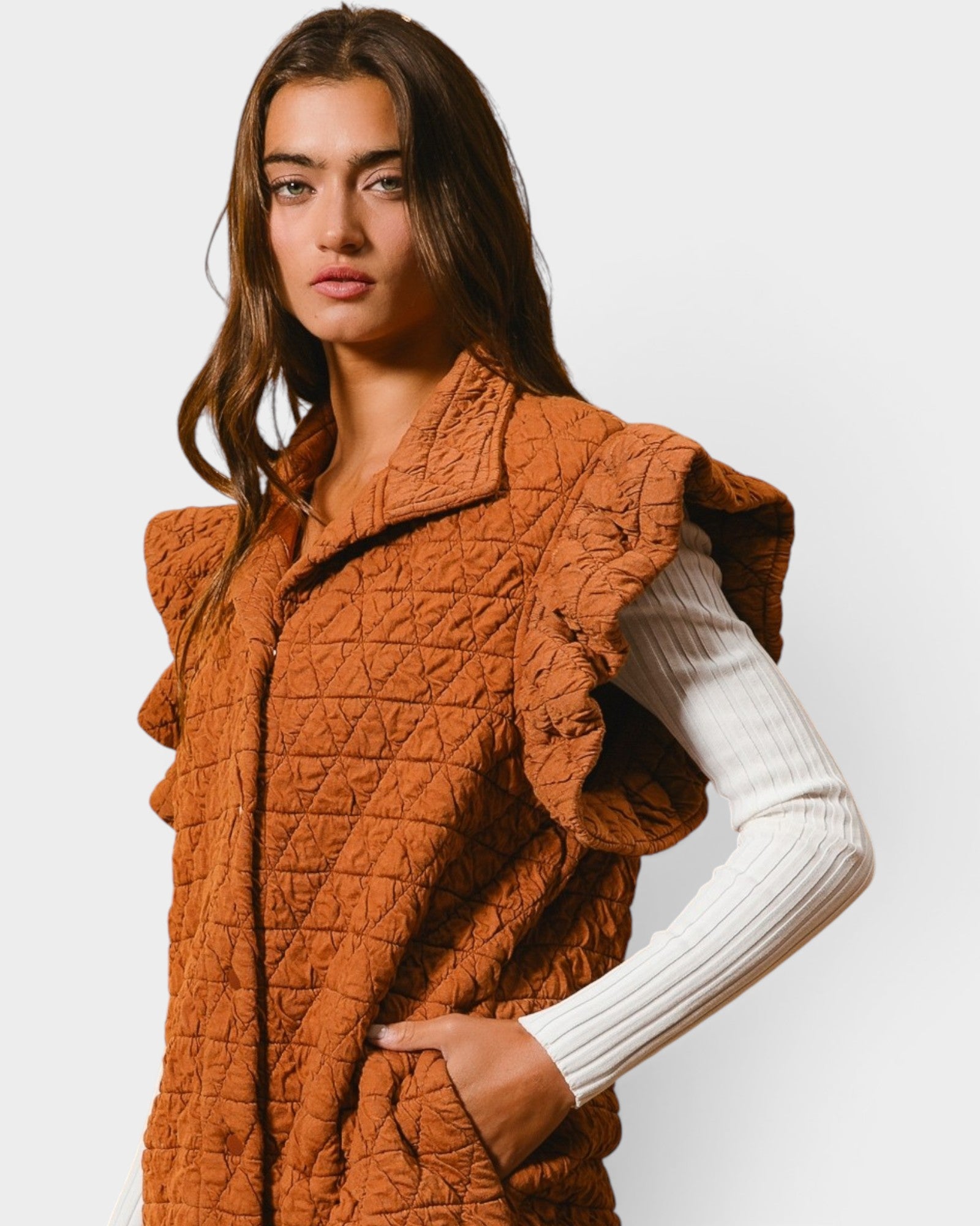 Woman wearing a brown quilted vest over a white sweater on a light gray background
