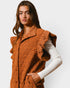 Woman wearing a brown quilted vest over a white sweater on a light gray background