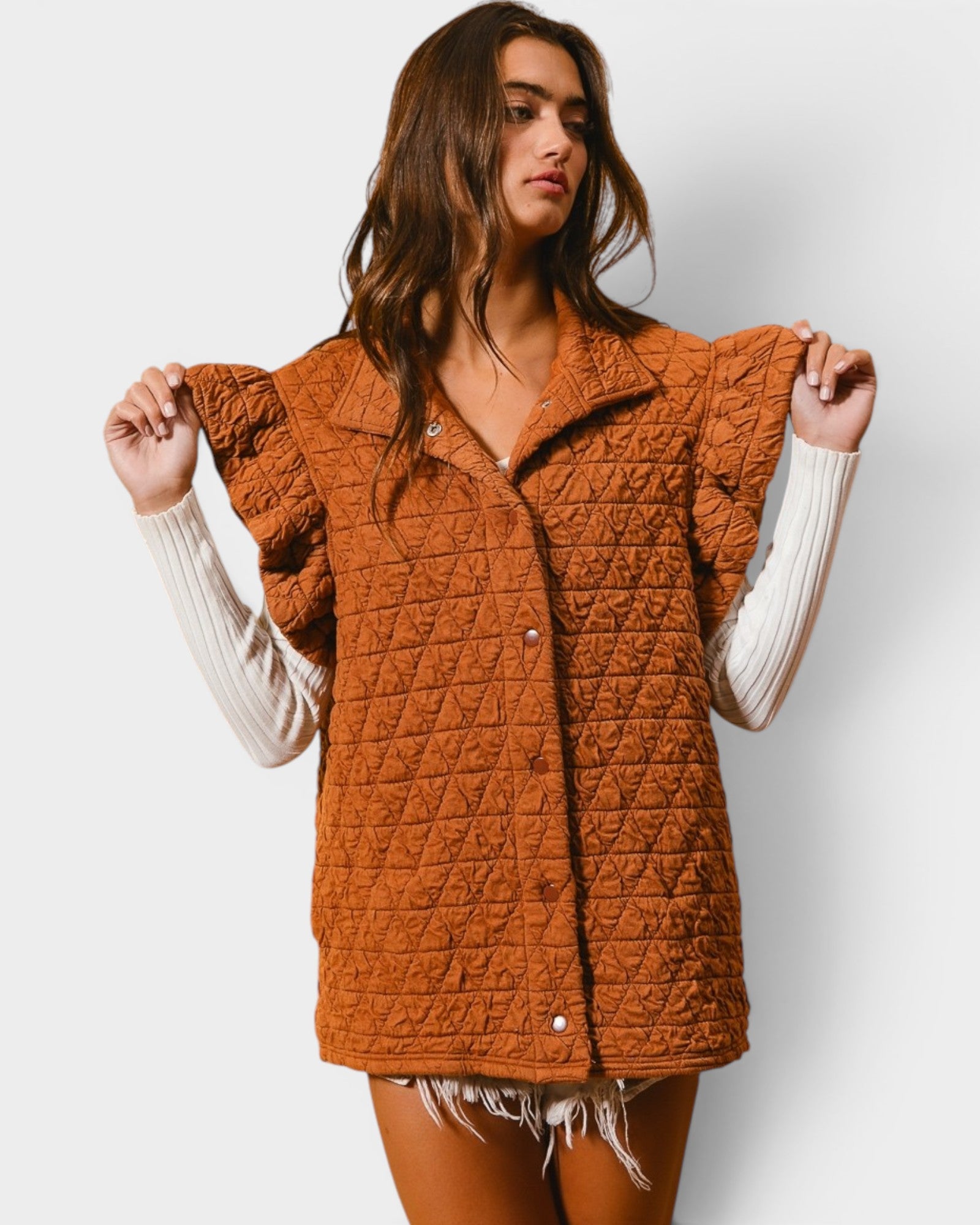 Woman wearing a brown quilted vest over a white long-sleeve shirt on a light gray background