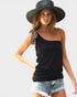 Woman wearing a black one-shoulder top, denim shorts, and a wide-brimmed hat on a plain background