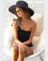 Woman wearing a black sun hat and black top sitting on a white chair.