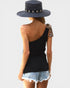 Person wearing a black one-shoulder top, denim shorts, and a straw hat with a white background
