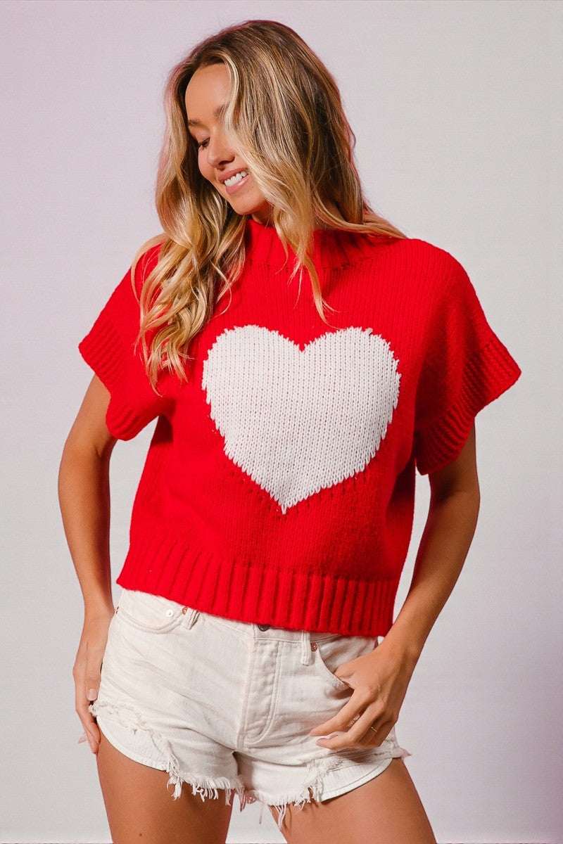 Woman wearing a red sweater with a white heart design on a plain background