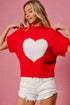Person wearing a red sweater with a white heart design on a pink background