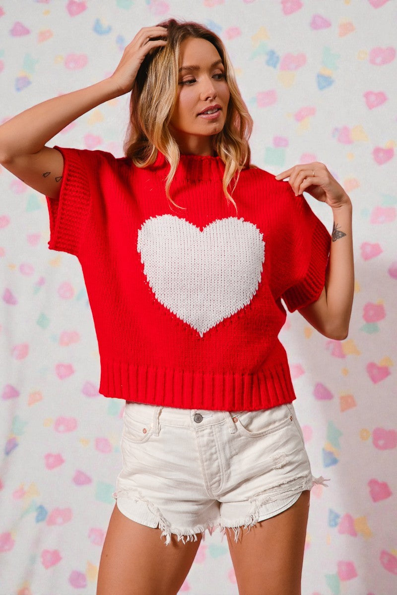 Woman wearing a red sweater with a white heart design against a colorful heart-patterned background
