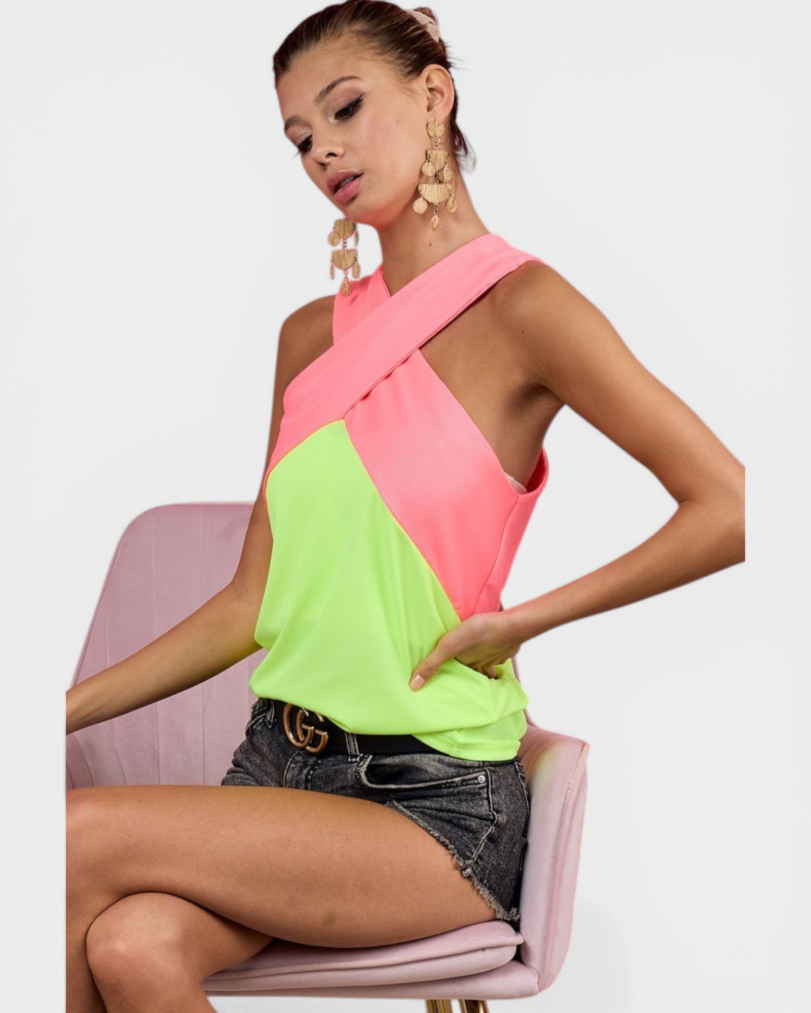 Woman wearing a pink and green top sitting on a pink chair with a white background