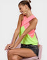 Woman wearing a neon green and pink top sitting on a pink chair.
