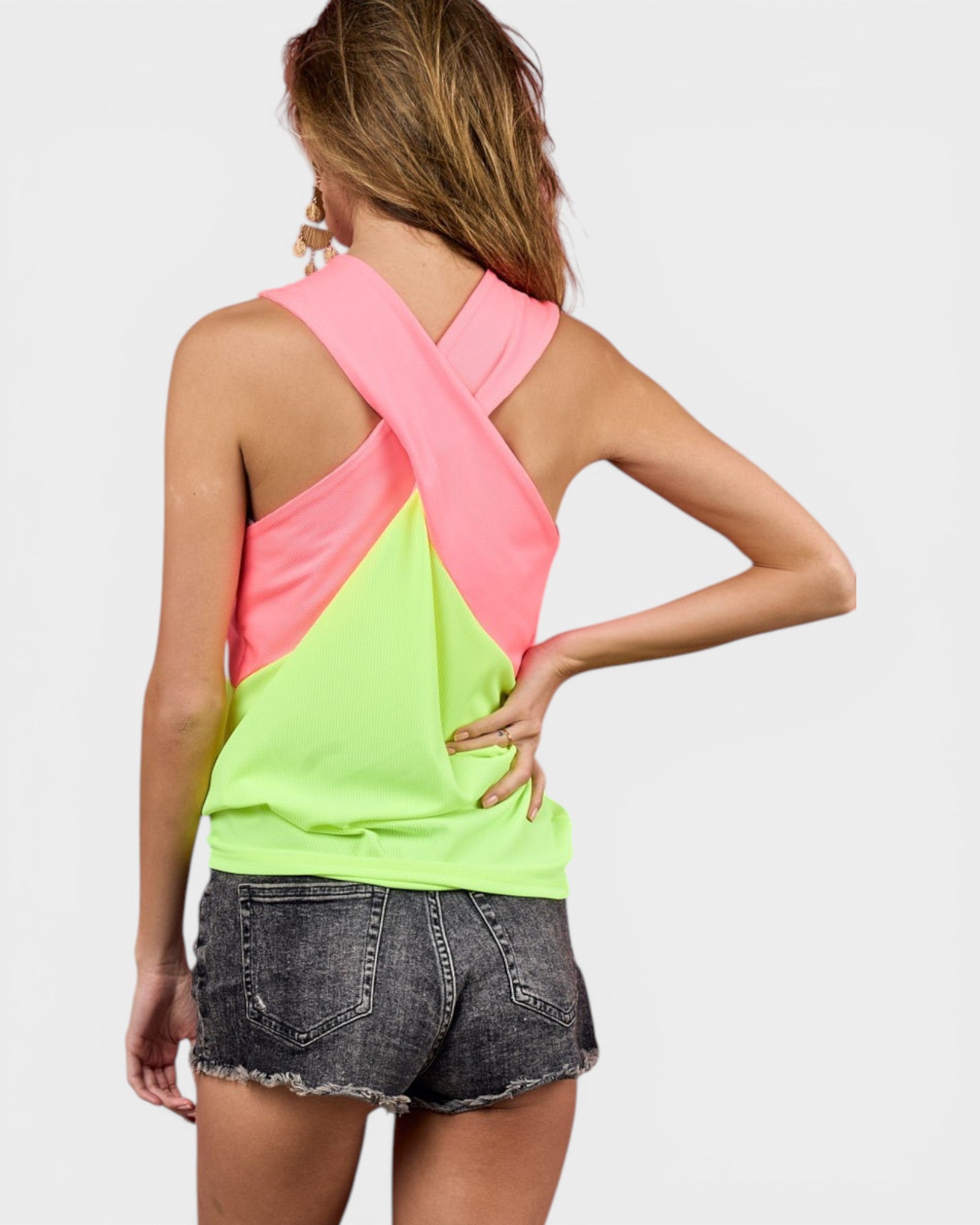 Woman wearing a neon green and pink cross-back top with denim shorts on a light gray background