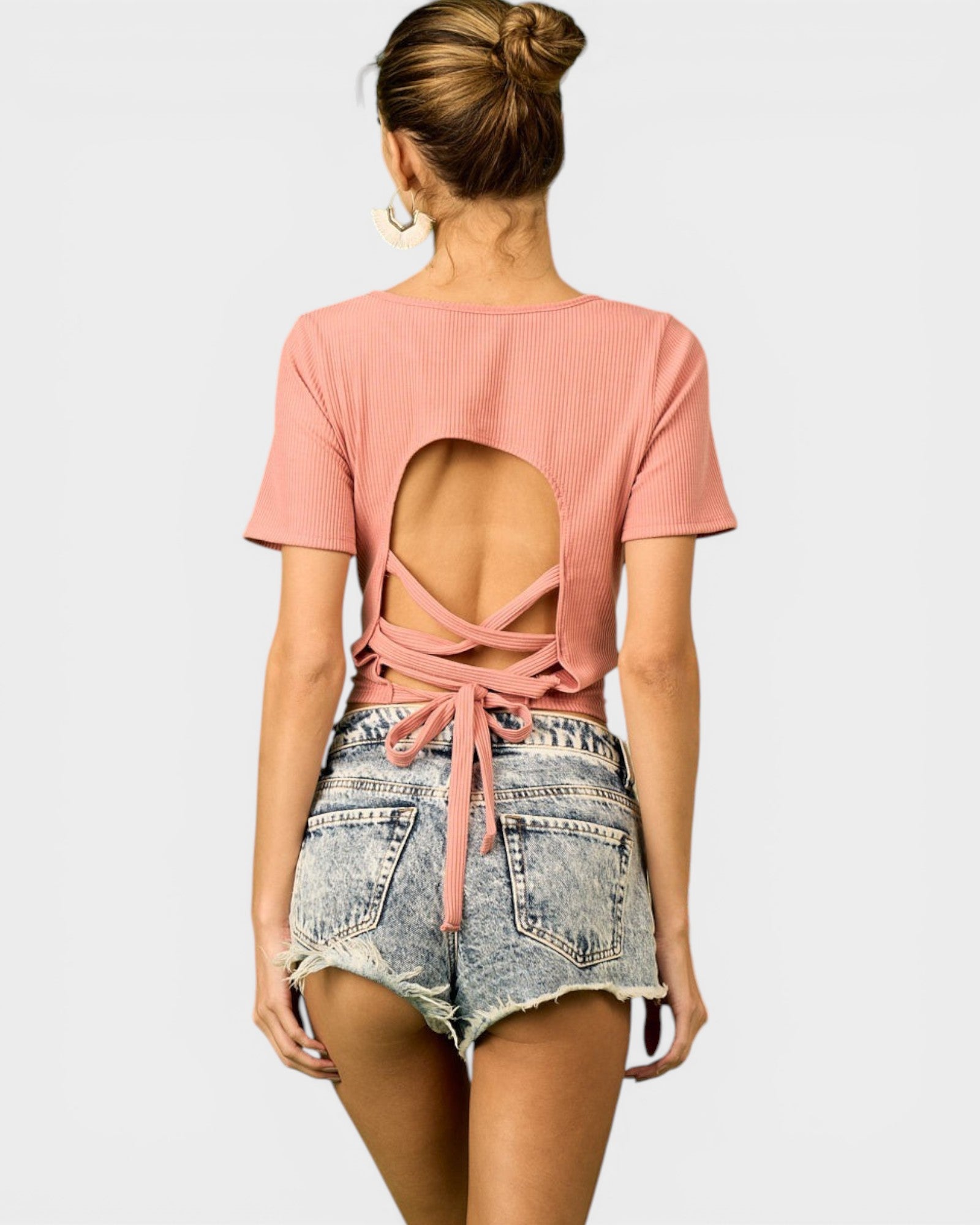 Woman wearing a pink open-back top and denim shorts on a white background