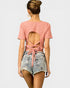 Woman wearing a pink open-back top and denim shorts on a white background