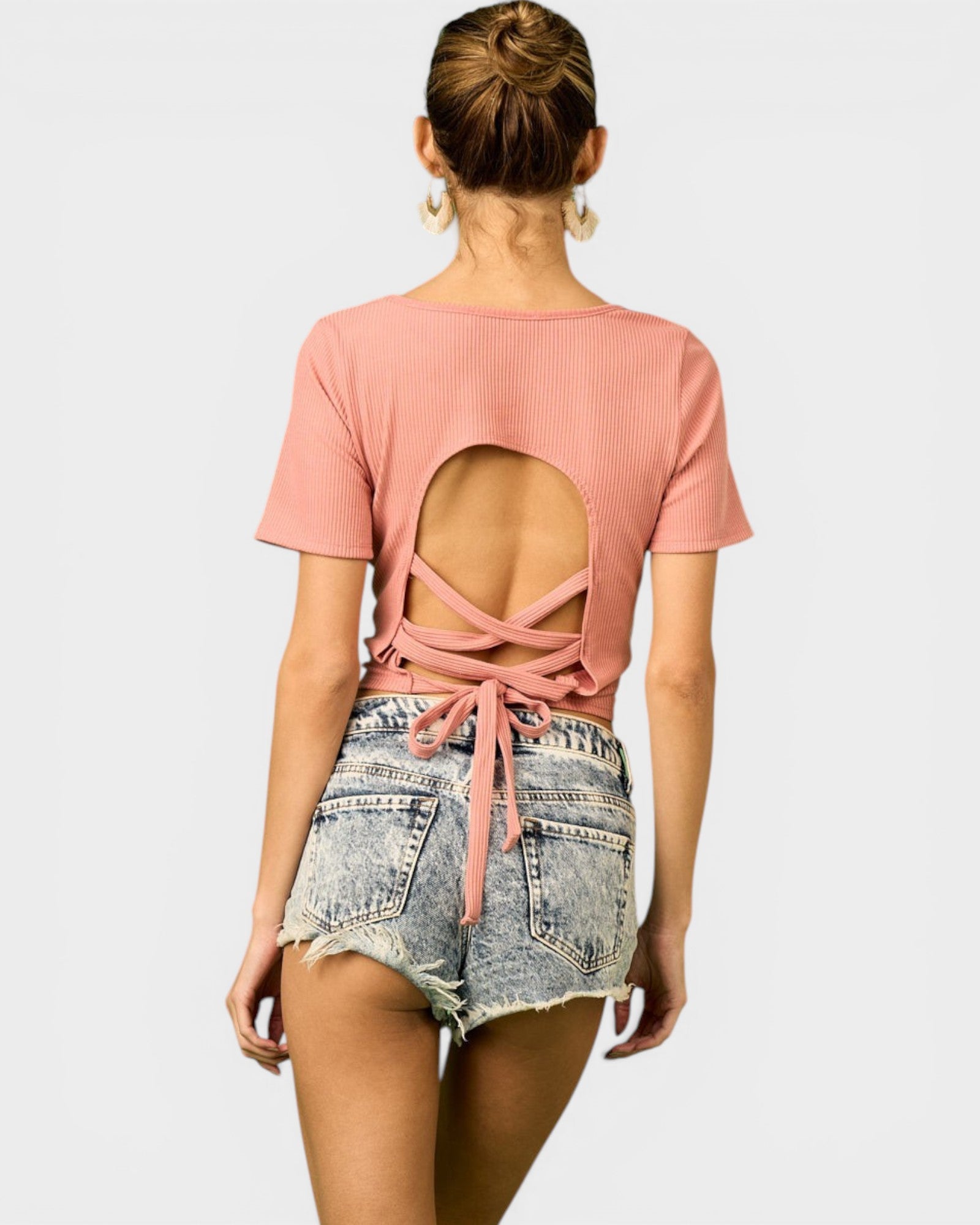 Person wearing a pink open-back top and denim shorts on a white background