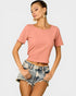 Woman wearing a pink ribbed crop top and denim shorts on a light gray background