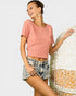 Woman wearing a pink top and denim shorts standing next to a woven basket on a light gray background