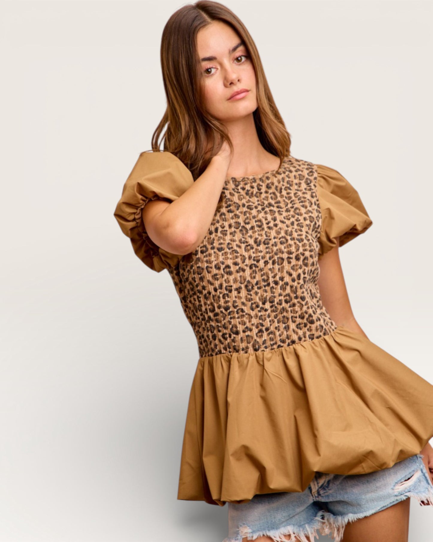Woman wearing a leopard print top with puff sleeves and a beige skirt on a white background