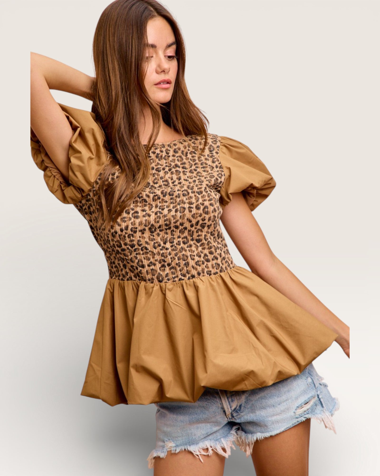 Woman wearing a leopard print top with puff sleeves and denim shorts on a light gray background