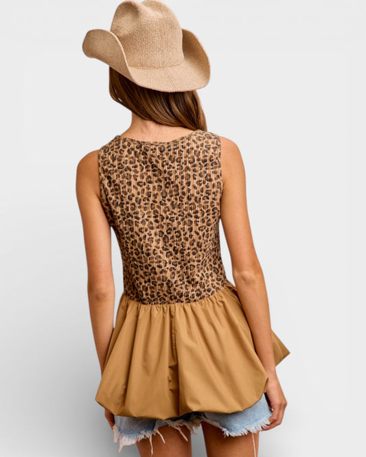 Person wearing a leopard print top and beige hat on a plain background