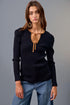 Woman wearing a black ribbed sweater with a brown tie and blue jeans against a gray background