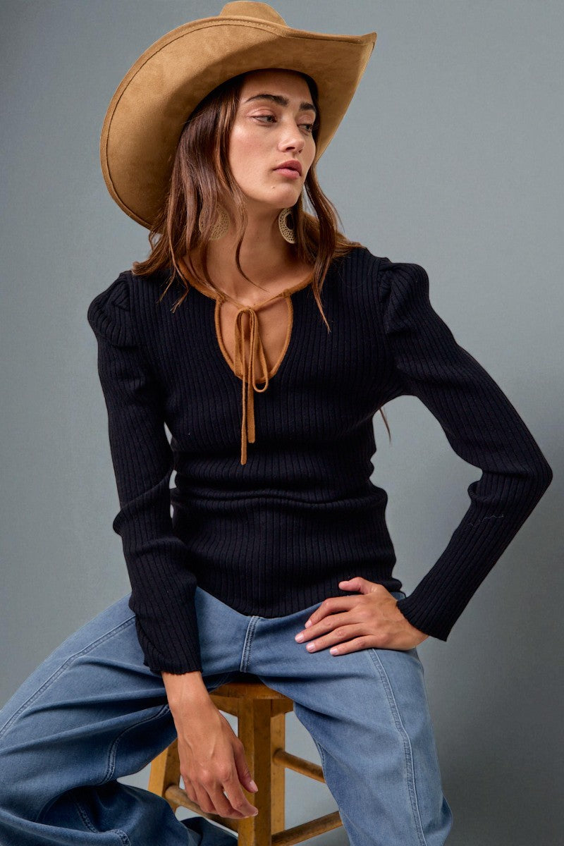 Woman wearing a black top, blue jeans, and a tan cowboy hat on a gray background