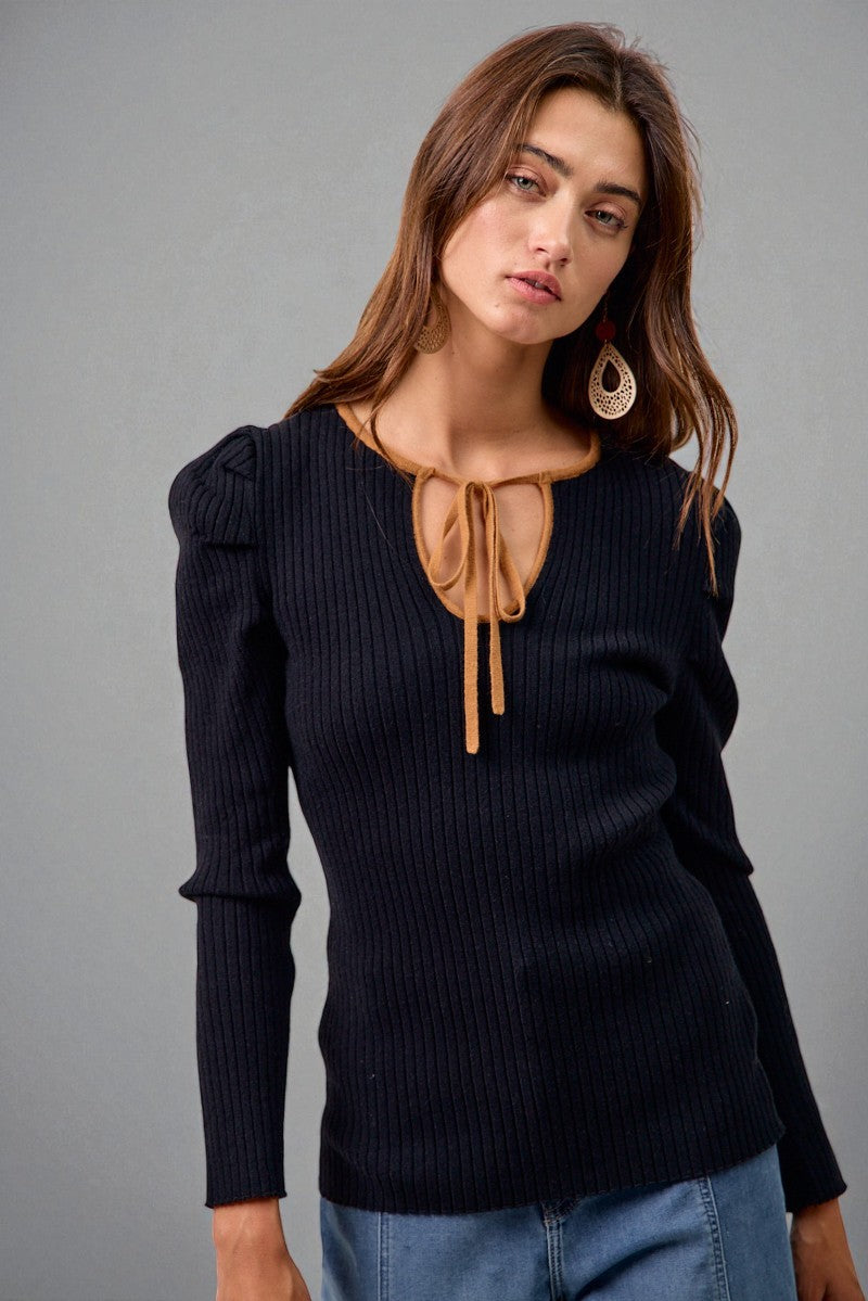 Woman wearing a black ribbed sweater with a tan bow detail on a gray background
