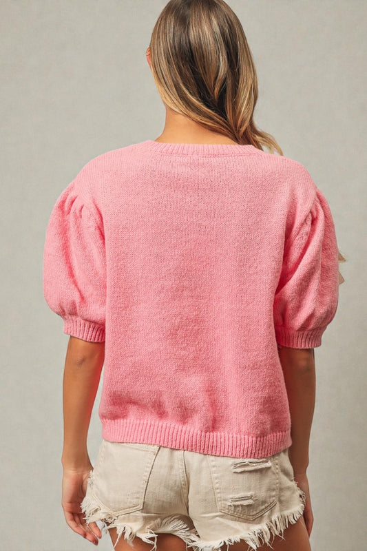 Person wearing a pink sweater with balloon sleeves against a neutral background