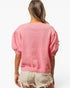 A woman shown from the back wearing a pink short-sleeve knit sweater with voluminous puff sleeves and beige frayed denim shorts against a plain white background.