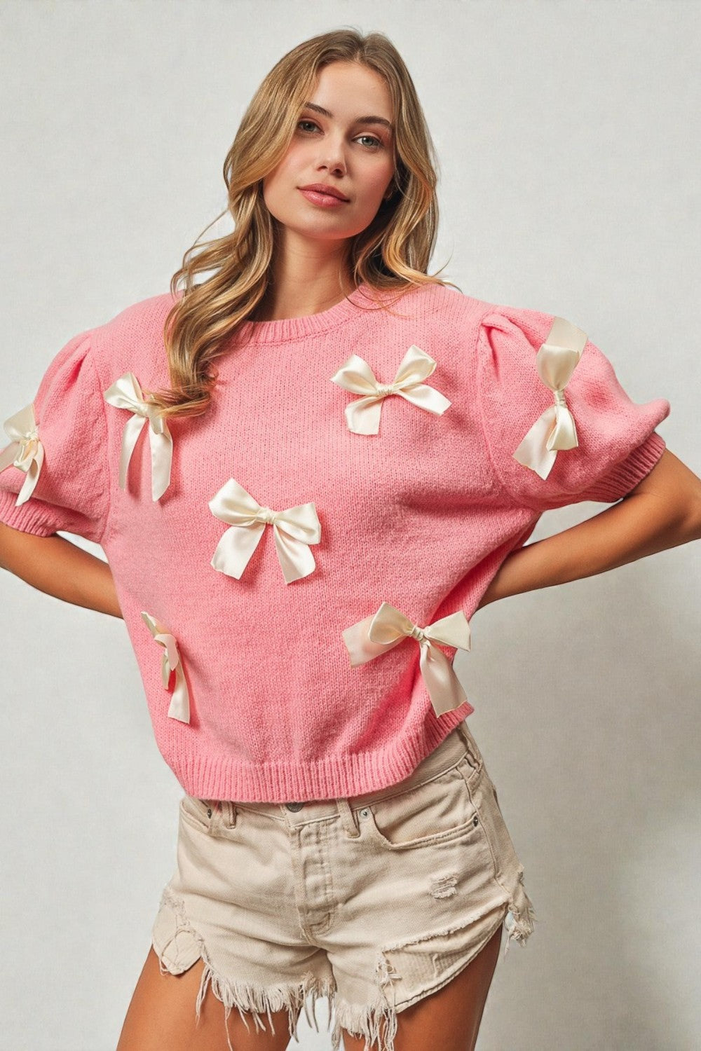 Woman wearing a pink sweater with bow details on a plain background