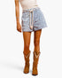 A model wearing light blue and white leopard-print western shorts with a beige rope drawstring, paired with brown cowboy boots and a beige knit top, shown from the waist down on a white studio background.