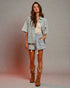 Woman wearing a floral outfit with cowboy boots against a plain background