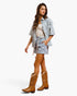 A woman modeling a matching western-style two-piece set featuring a blue and white floral print short-sleeve shirt and shorts with a drawstring waist, paired with brown cowboy boots against a plain white background.
