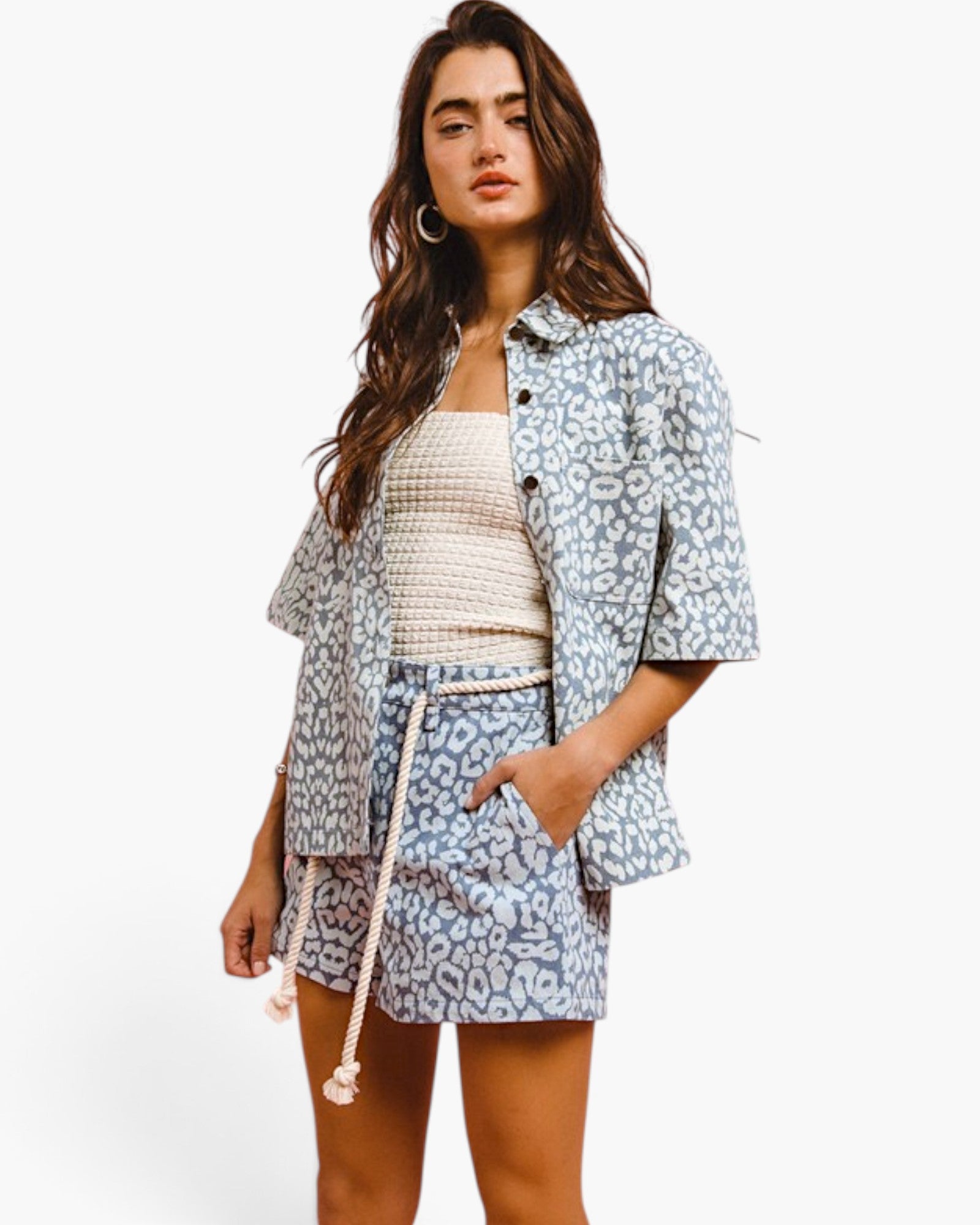 A woman modeling a matching light blue and white patterned short-sleeve button-up shirt and shorts set with a cream knit top, against a plain white studio background.