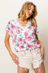 Woman wearing a floral top and white shorts against a plain background