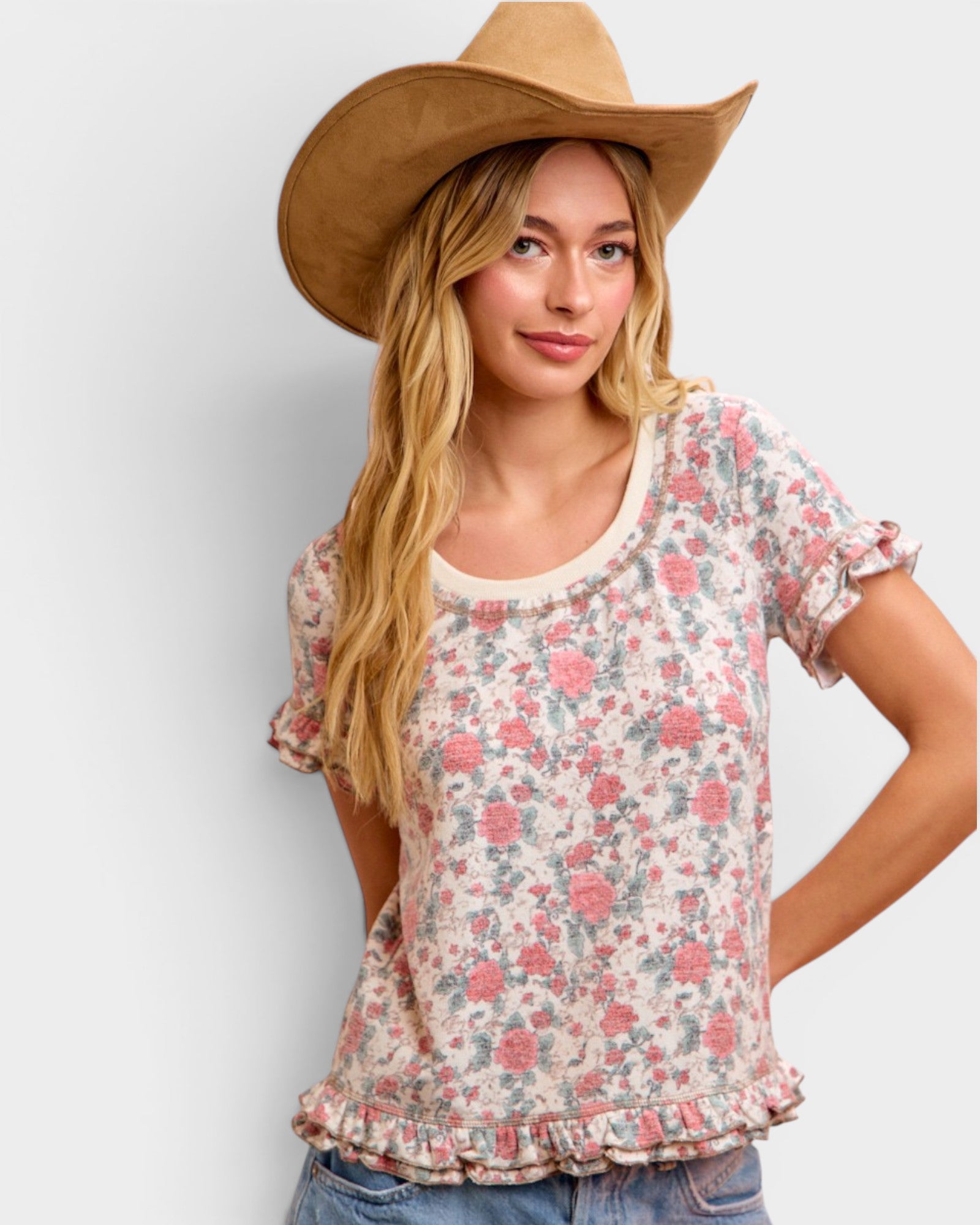 Woman wearing a floral blouse and wide-brimmed hat against a plain background