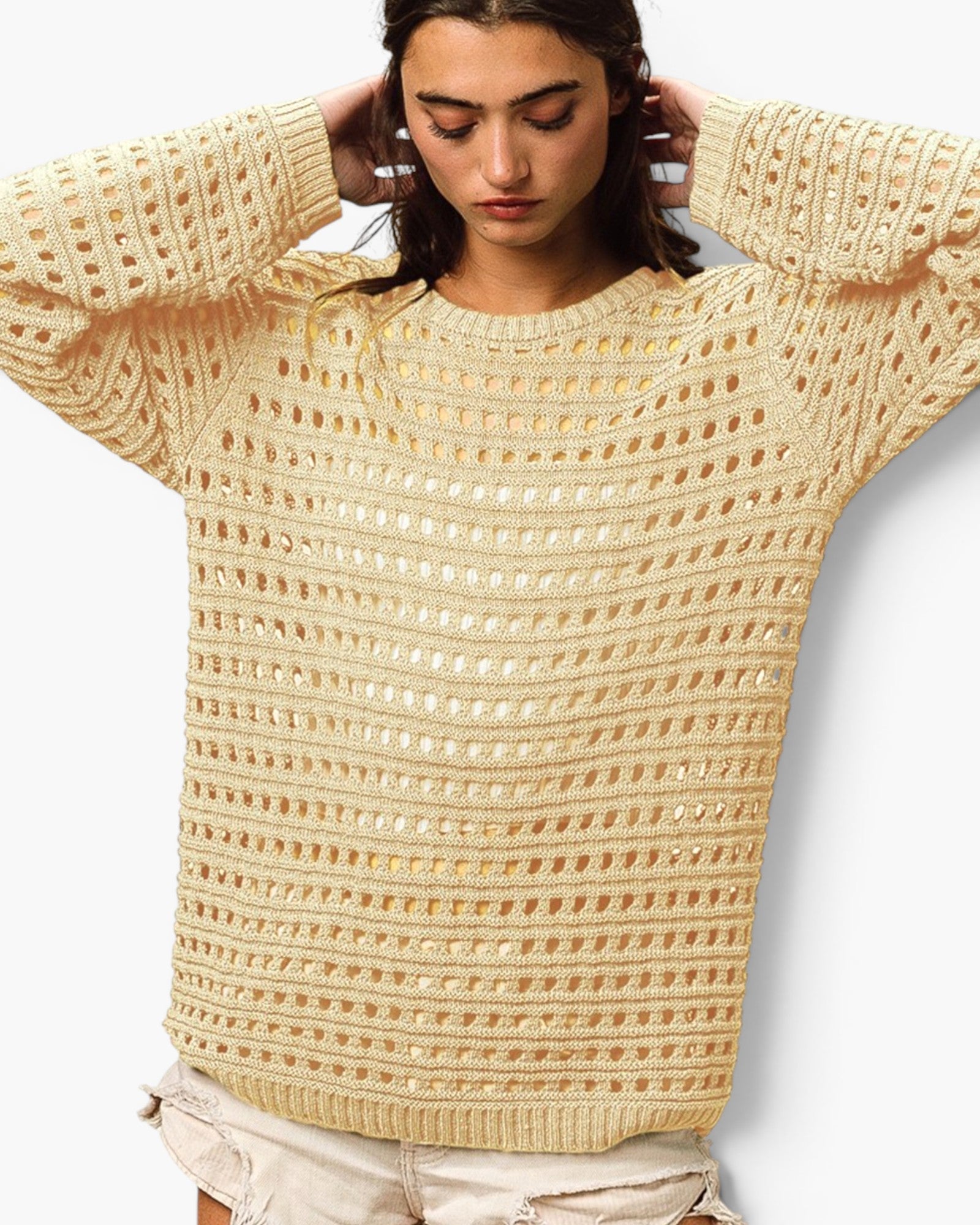 A woman wearing a cream-colored, open-knit crewneck sweater with textured horizontal rows, paired with light beige shorts, against a plain white background.