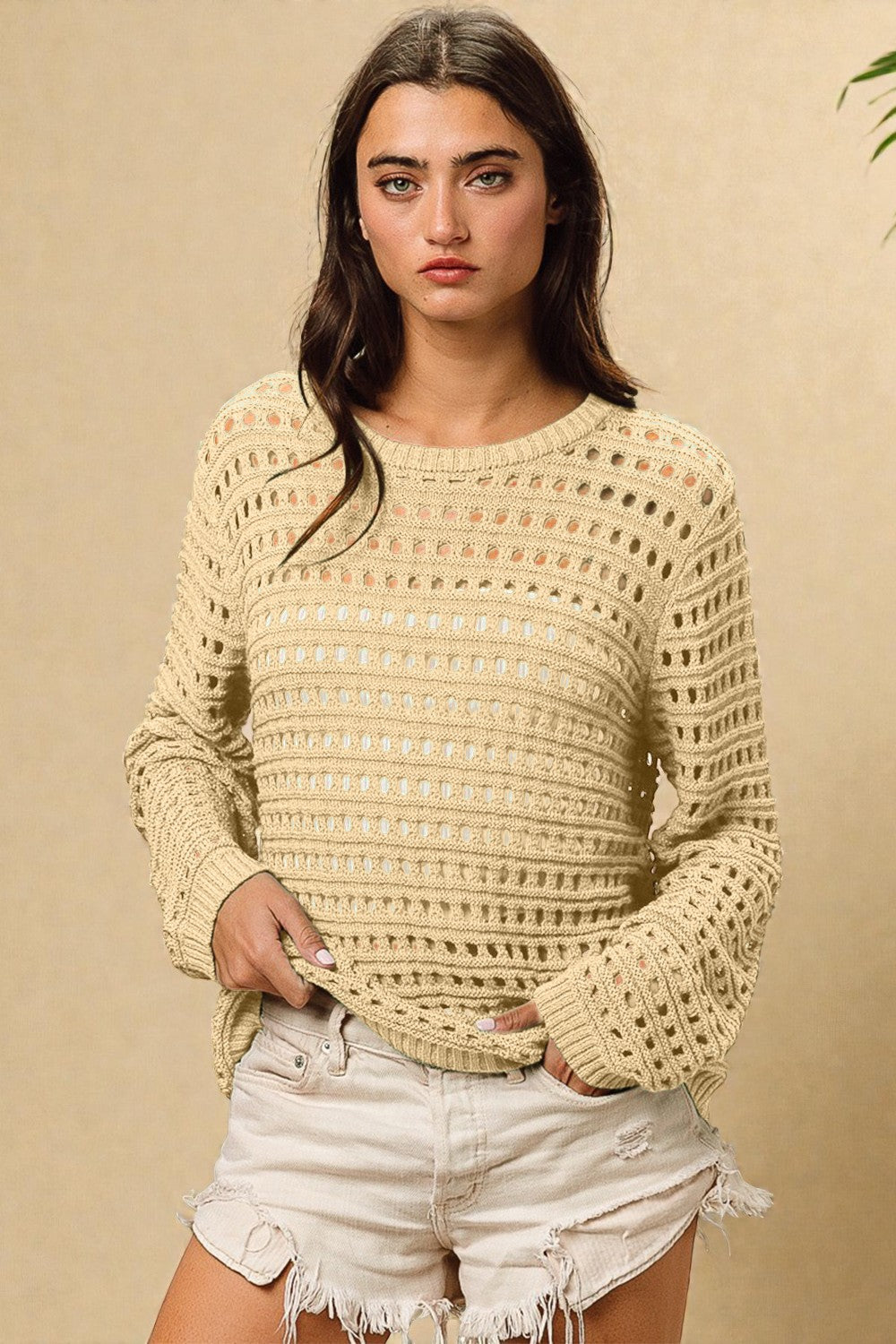 Woman wearing a beige crochet sweater and white shorts against a beige background
