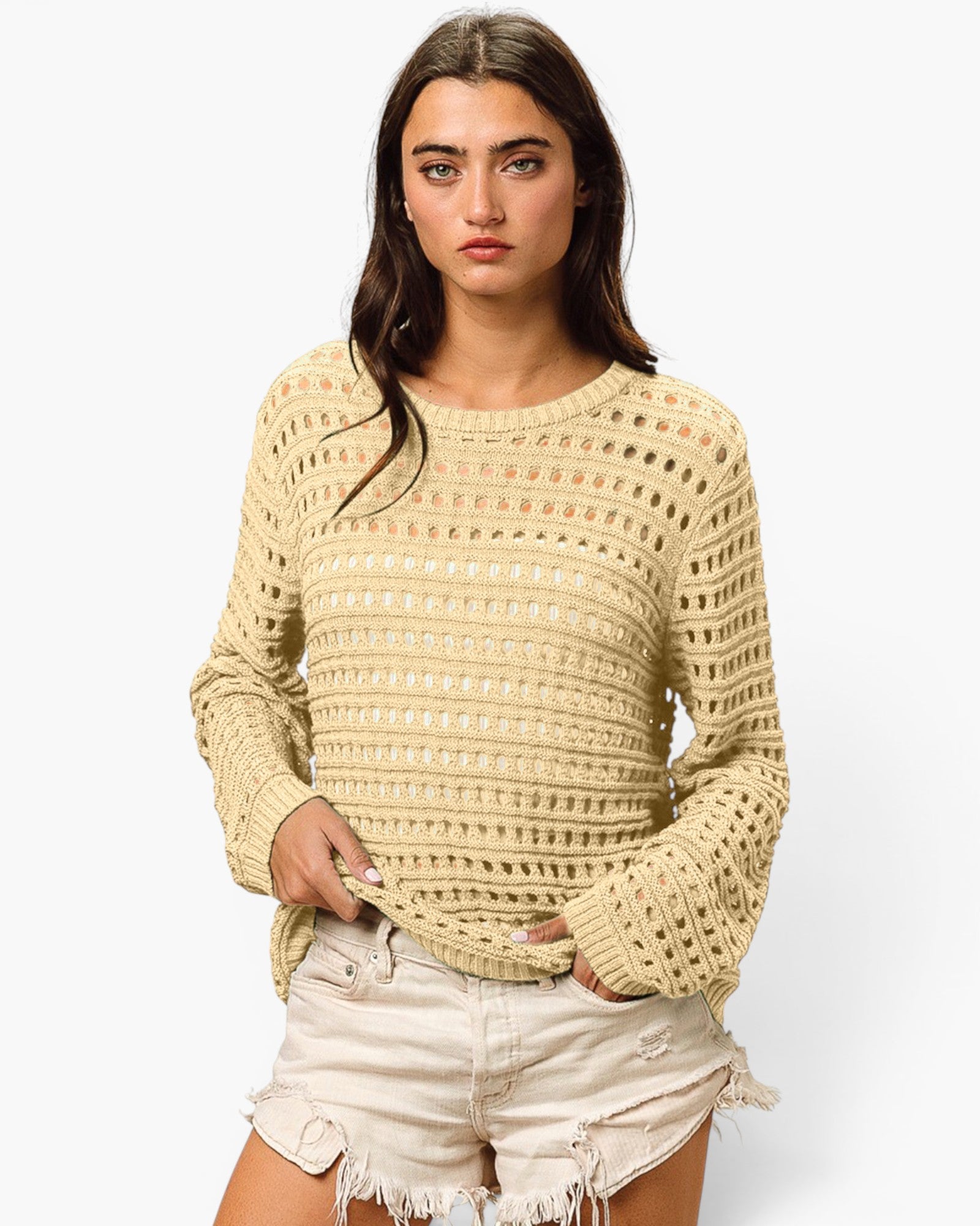 A woman modeling a cream-colored open-knit long-sleeve sweater paired with light-wash frayed denim shorts against a plain white background.