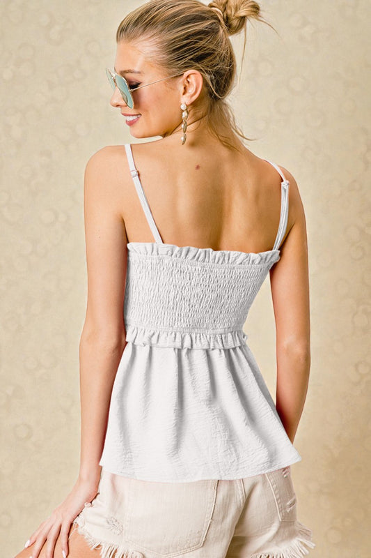 Woman wearing a light gray smocked top with thin straps against a beige background