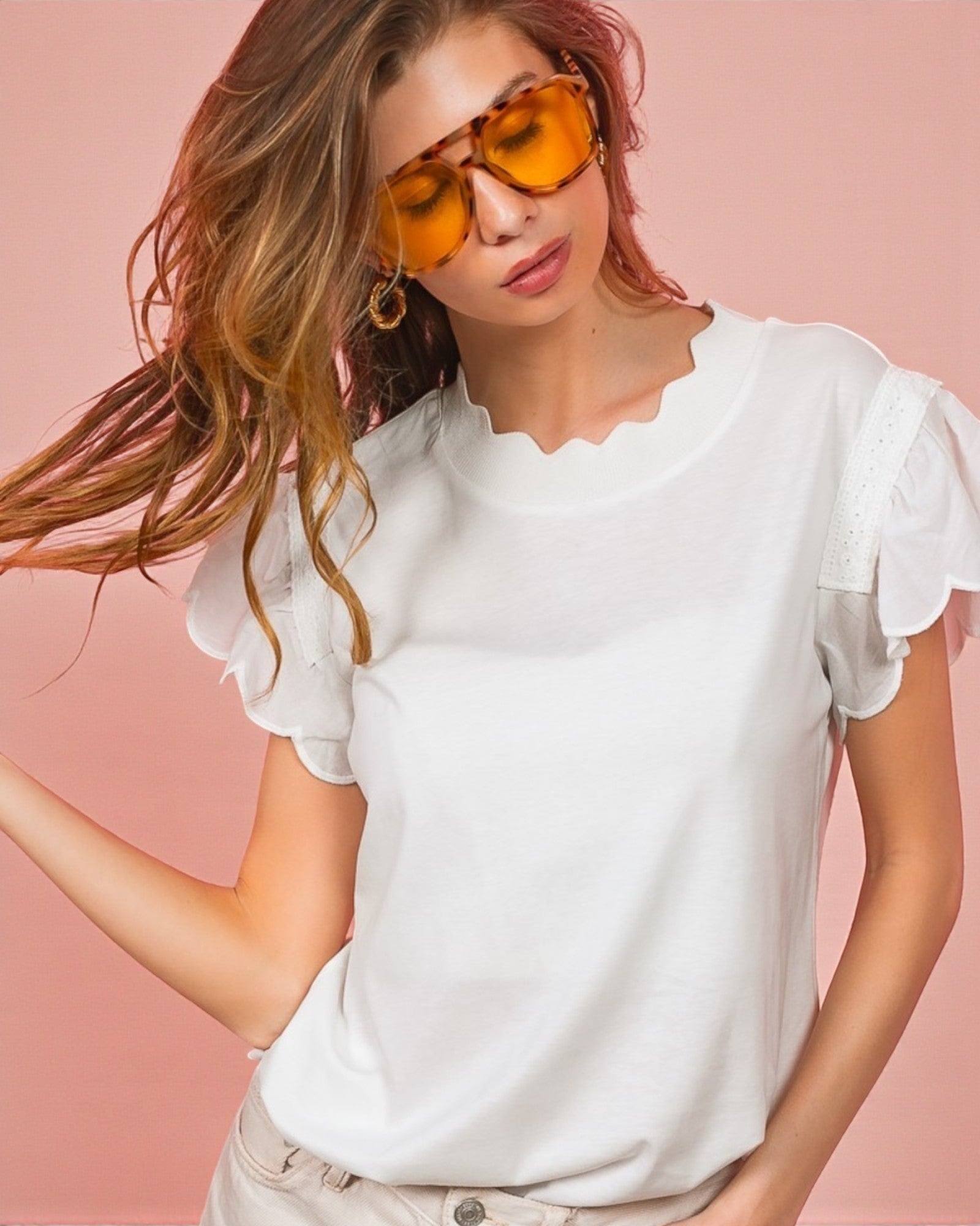 Woman wearing a white blouse with ruffled sleeves against a pink background