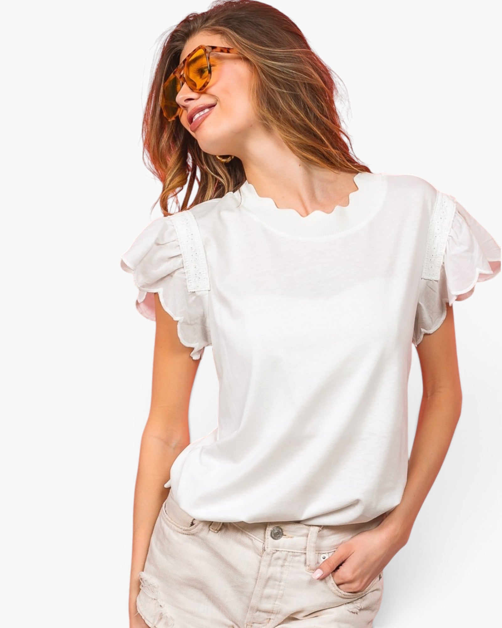 A woman wearing a white short-sleeve blouse with ruffled flutter sleeves and a scalloped neckline, paired with light beige shorts, against a plain white background.