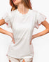 A woman wearing a white short-sleeve top with ruffled flutter sleeves and a scalloped neckline, paired with light beige shorts, against a plain white background.