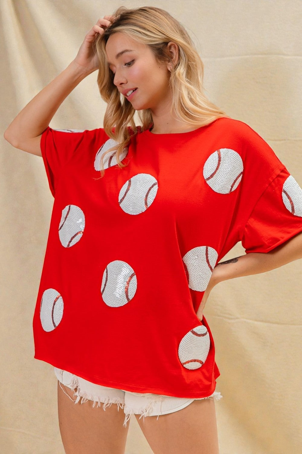 Woman wearing a red oversized t-shirt with white baseball patterns on a beige background