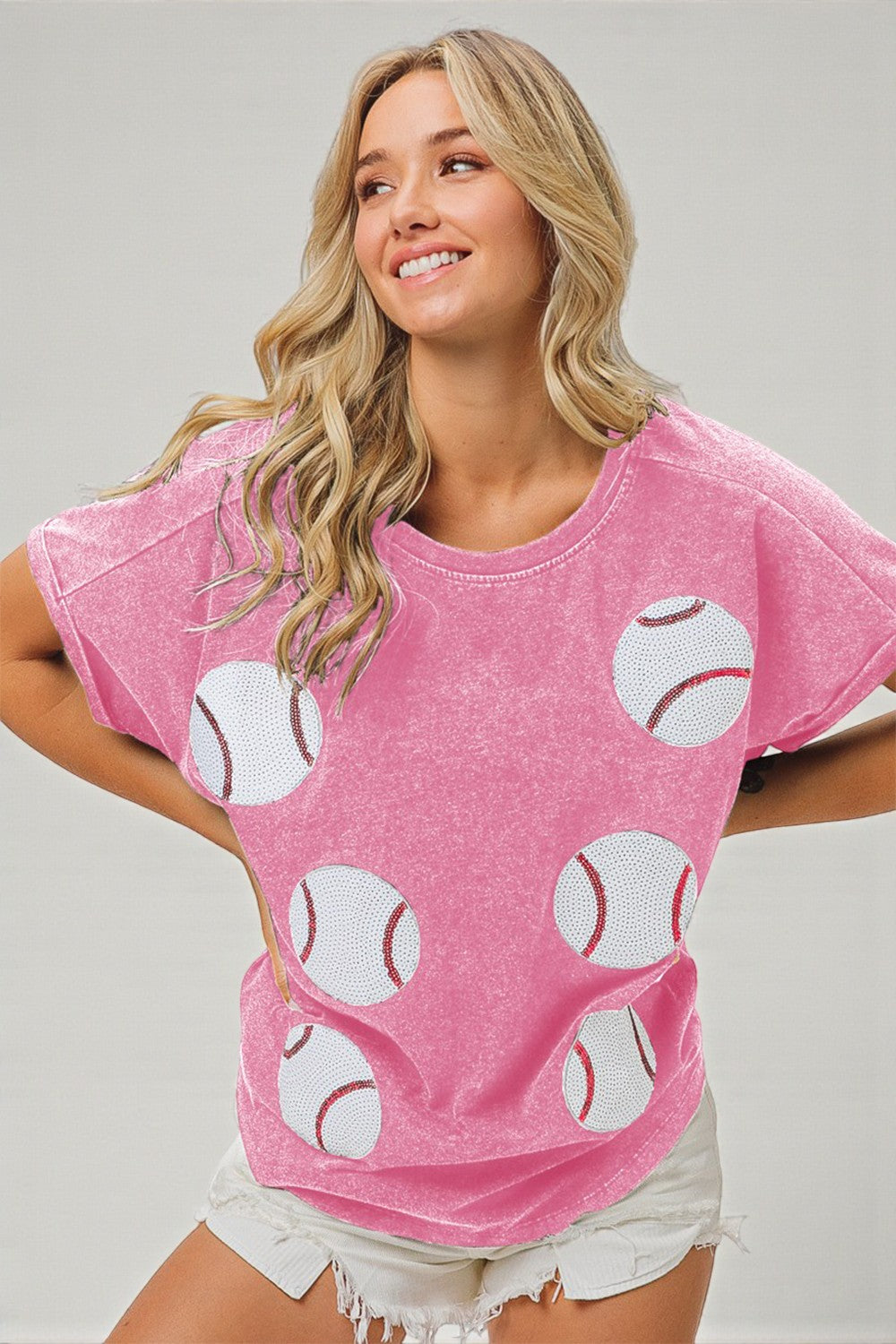 Woman wearing a pink t-shirt with baseball patterns on a plain background