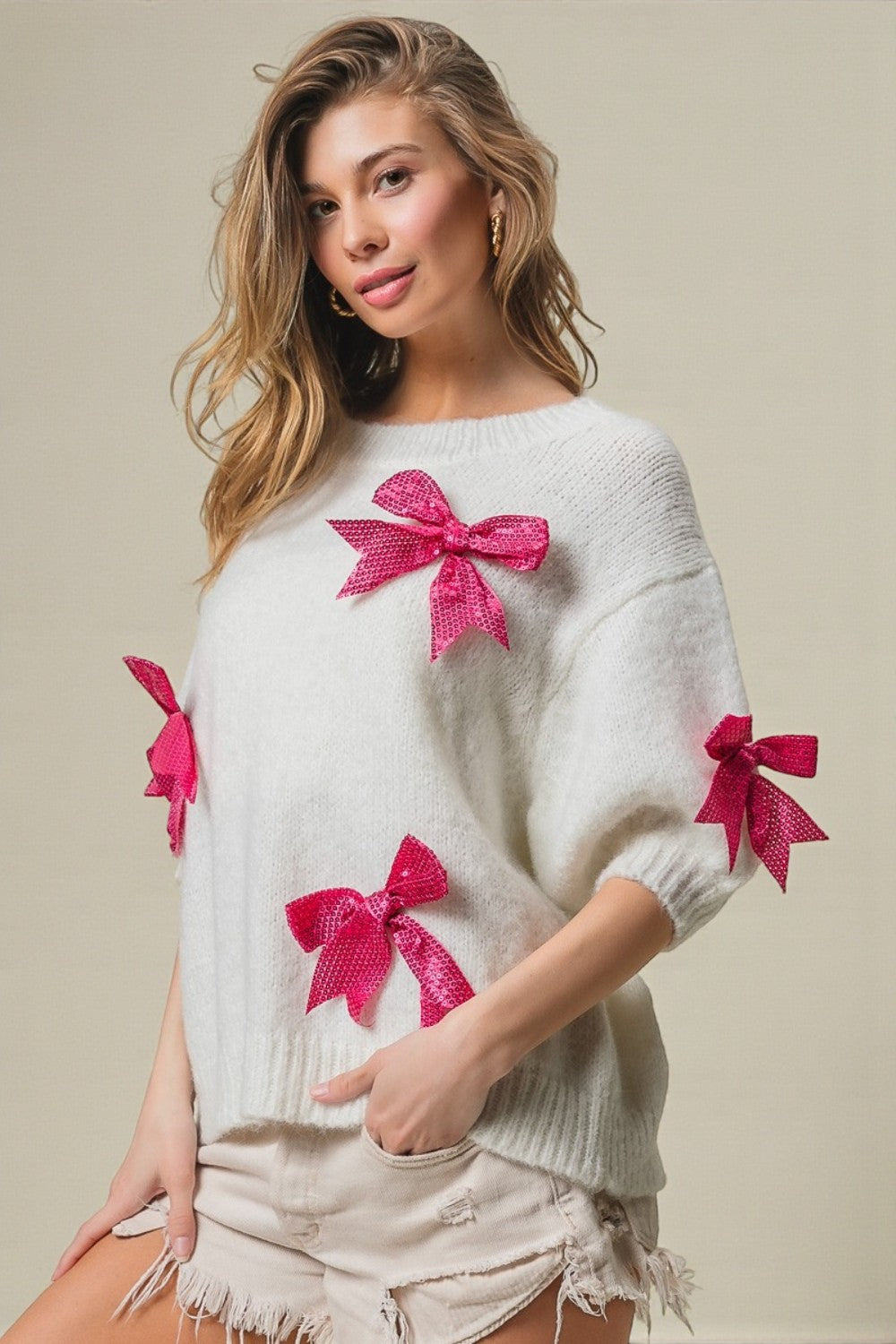 Woman wearing a white sweater with pink bows on a beige background