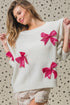 Woman wearing a white sweater with pink bows against a patterned background