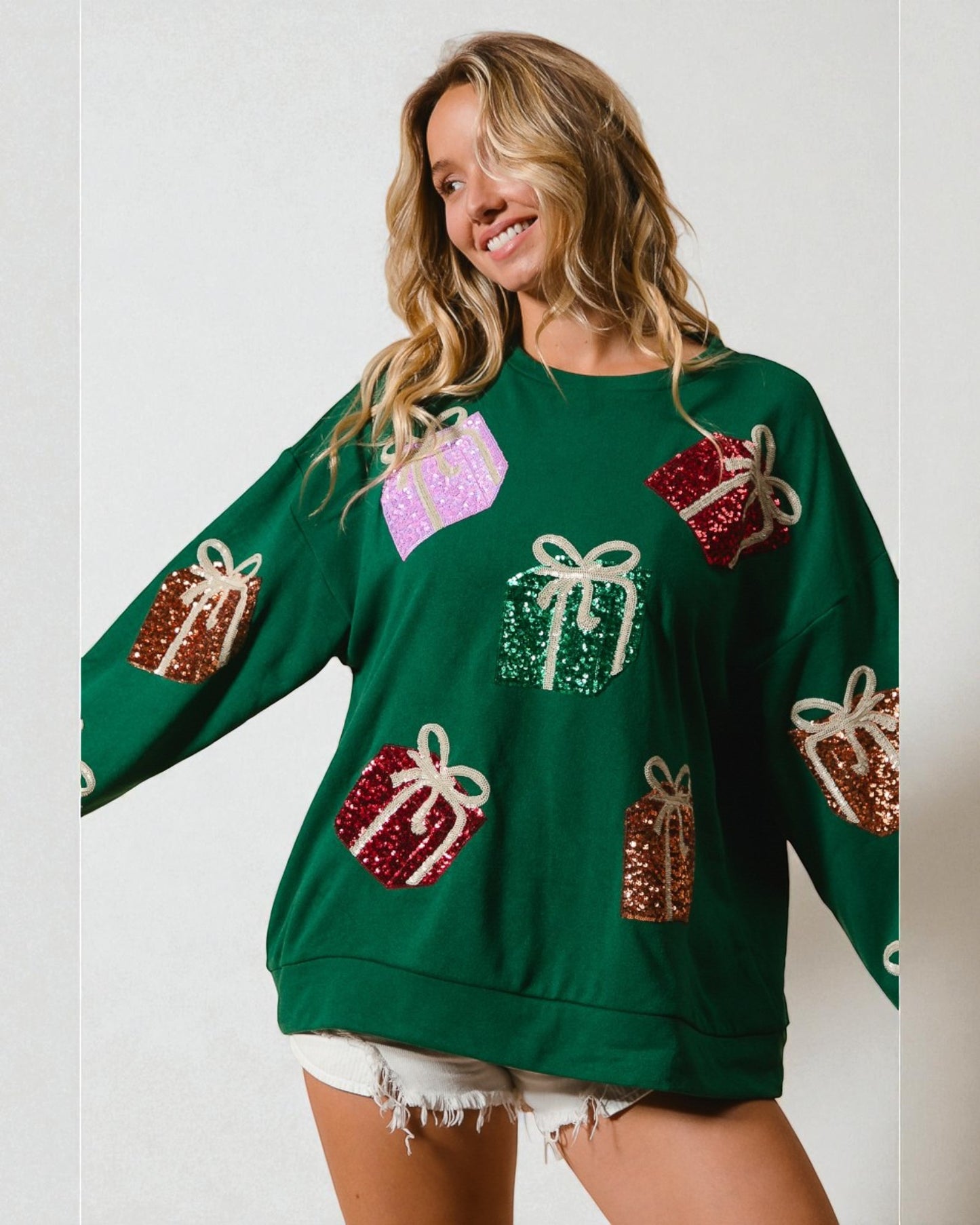 Woman wearing a green sweater with decorative gift patterns on a plain background