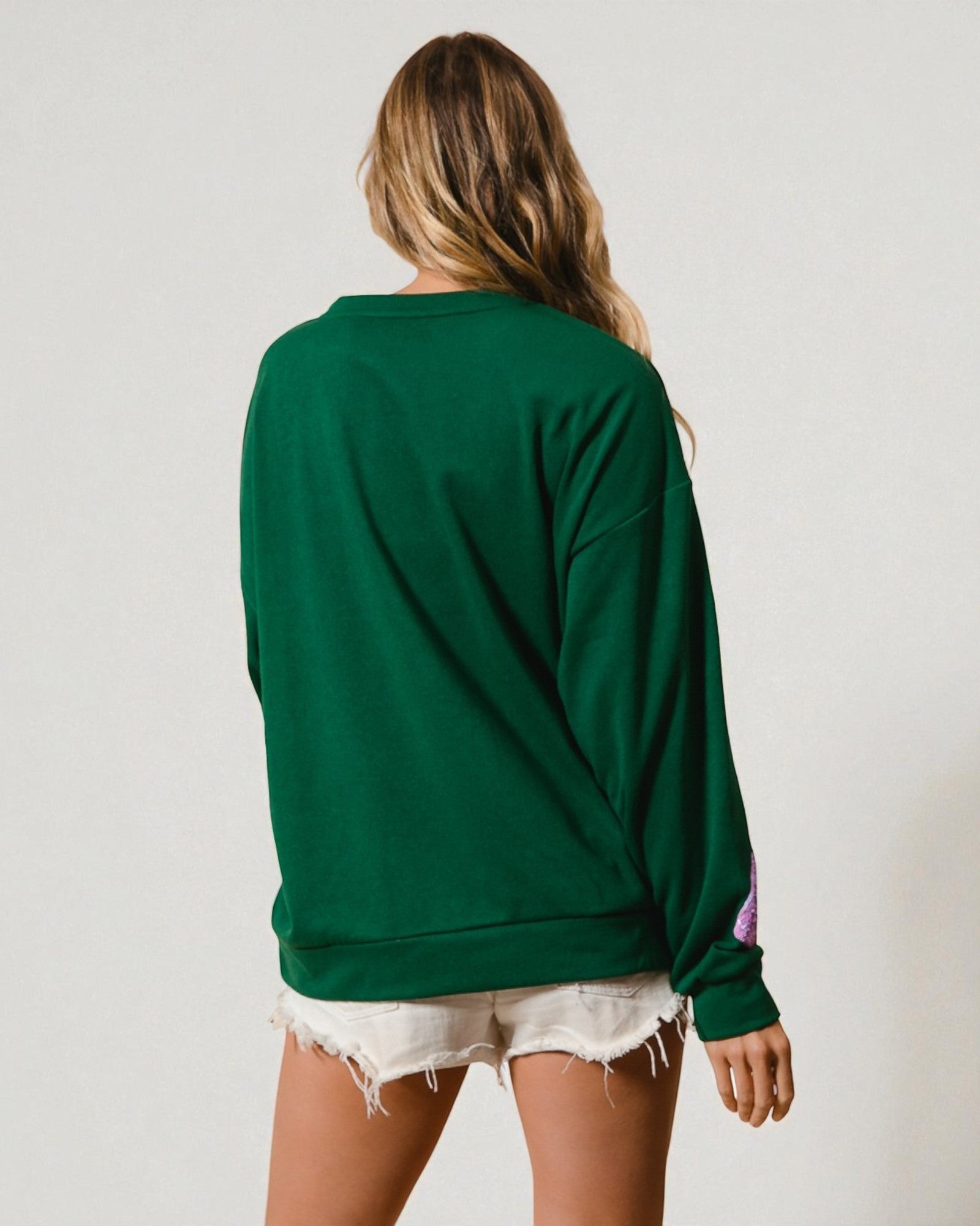 Person wearing a green sweatshirt and white shorts on a plain background