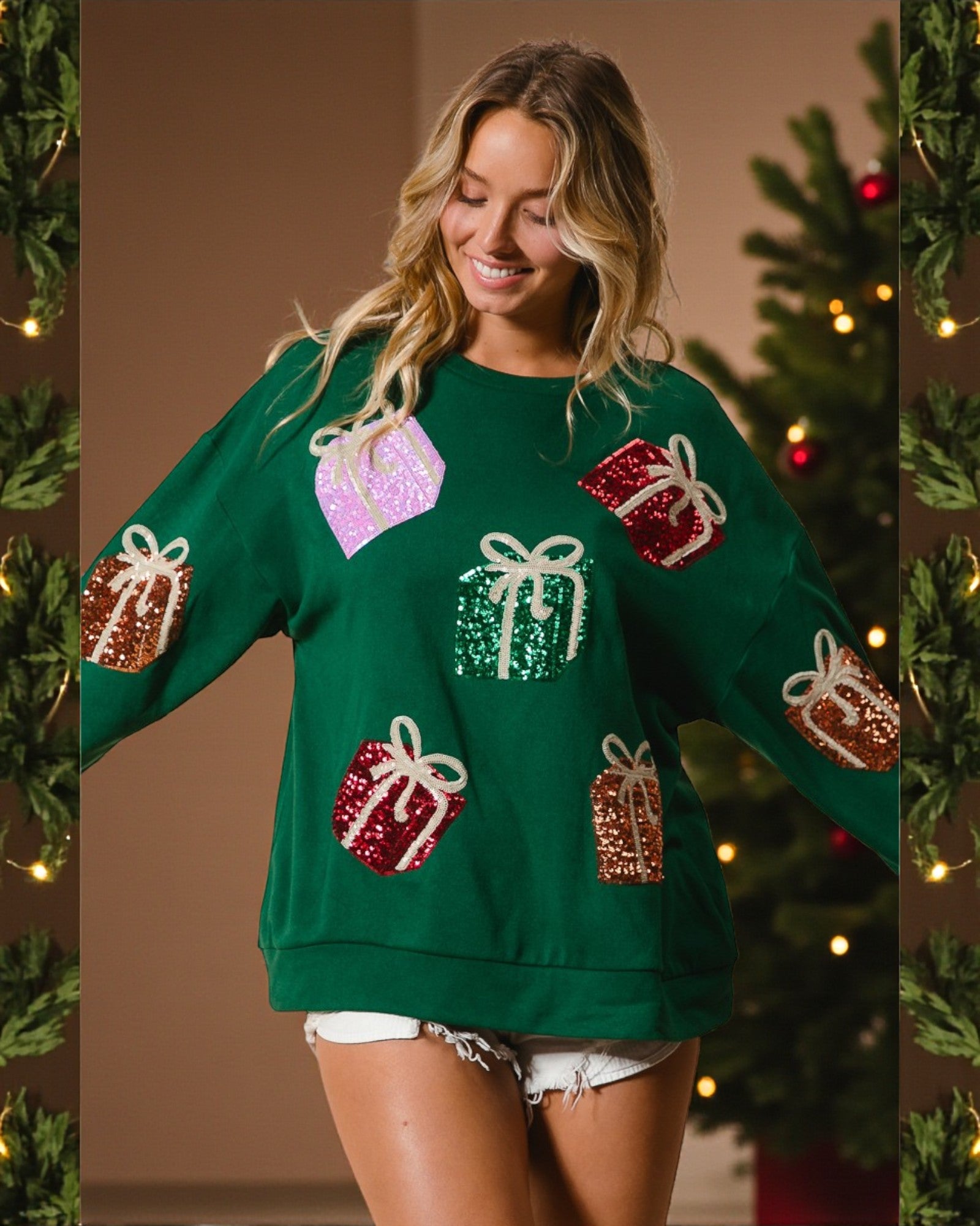 Woman wearing a green sweater with festive gift designs in front of a decorated Christmas tree.