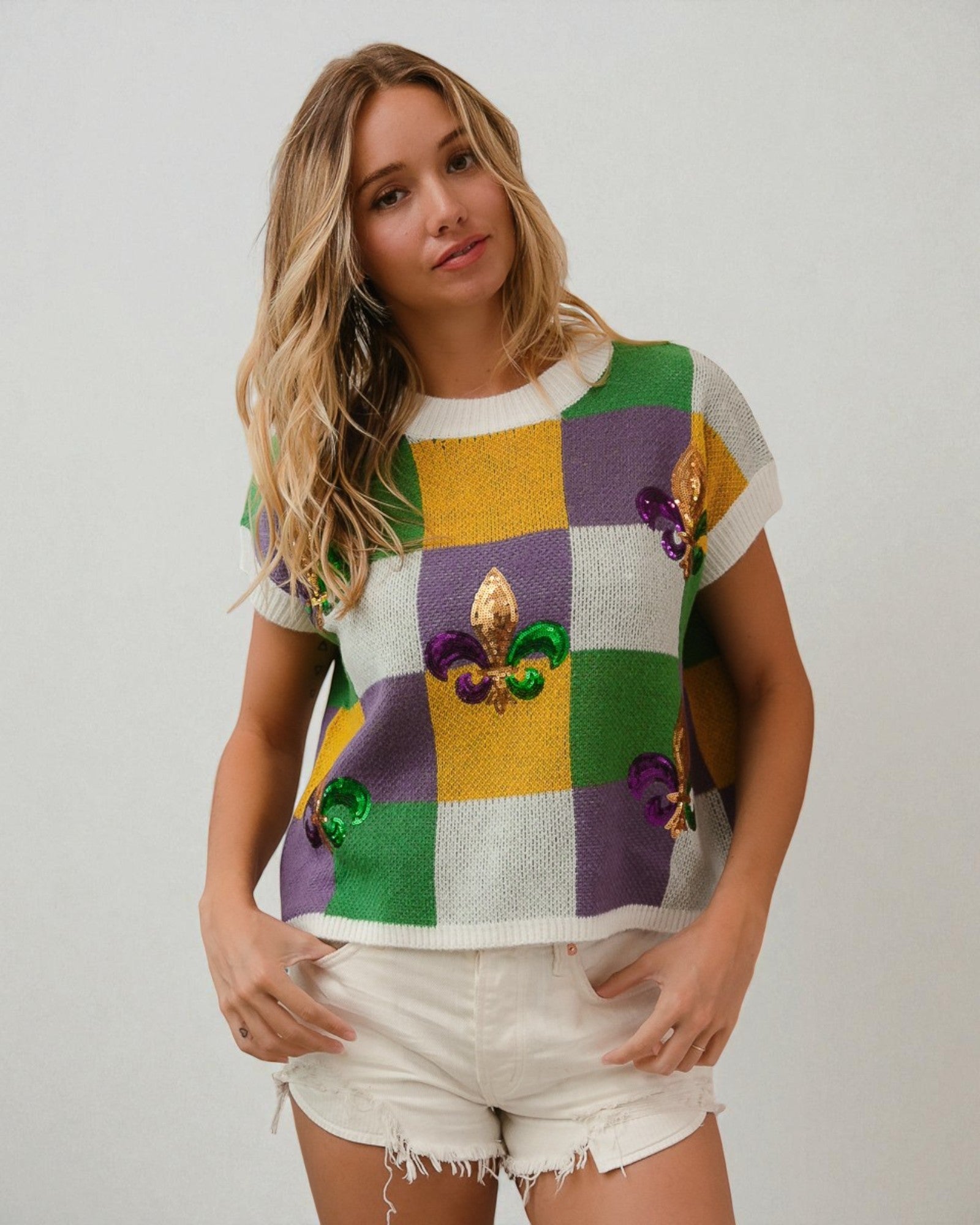 Woman wearing a colorful checkered sweater with floral embellishments on a plain background