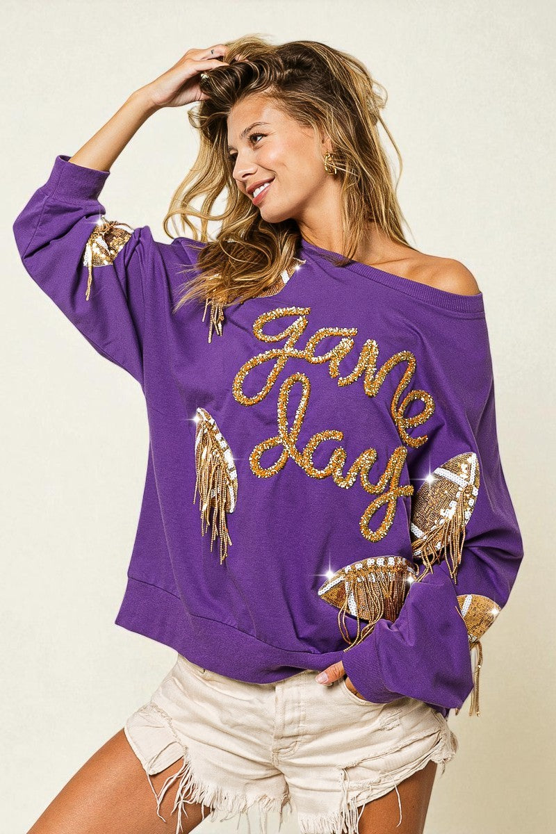 Woman wearing a purple sweatshirt with 'Game Day' text and gold fringe details on a plain background