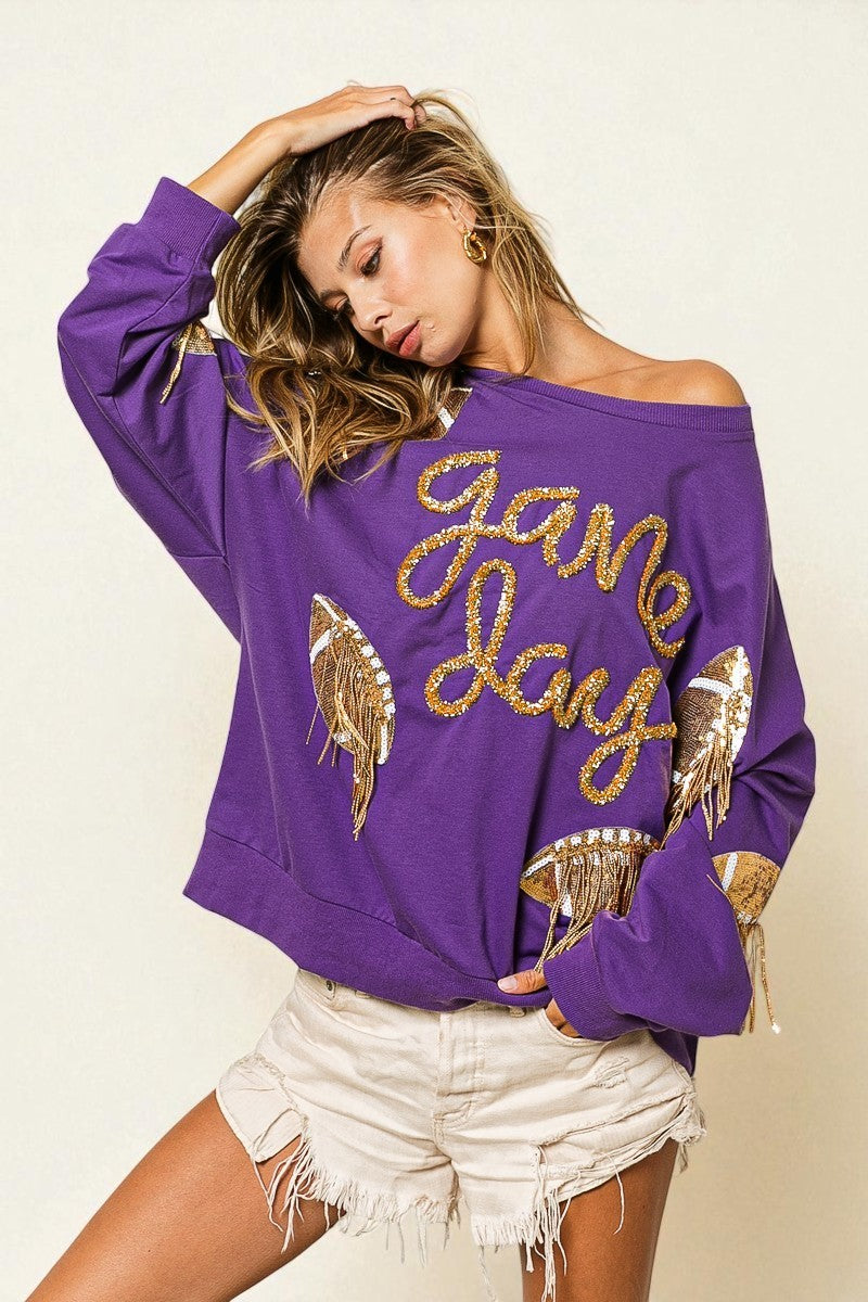 Woman wearing a purple sweatshirt with 'Game Day' and angel wings design on a plain background